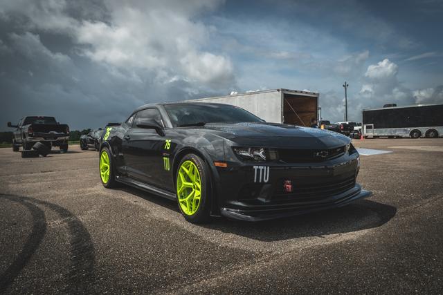 Black Camaro with lime green wheels in a paddock under dramatic sky