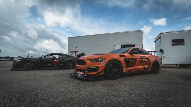 Orange Shelby GT350 in a track paddock under dramatic storm clouds