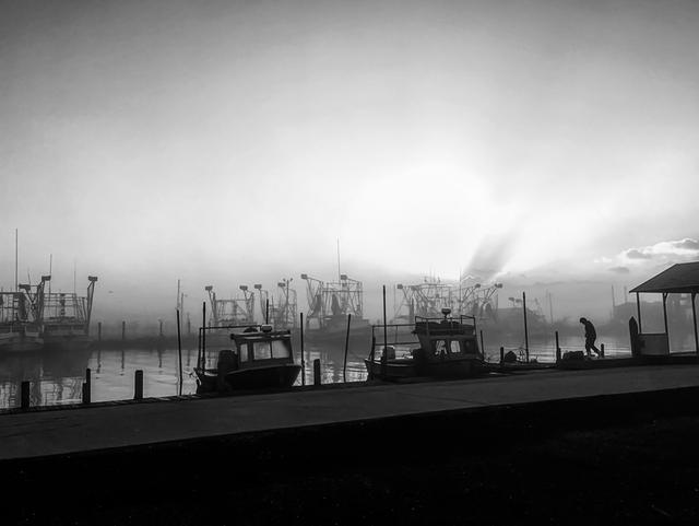 Black and white view of shrimp boats docked in a foggy harbor at sunrise