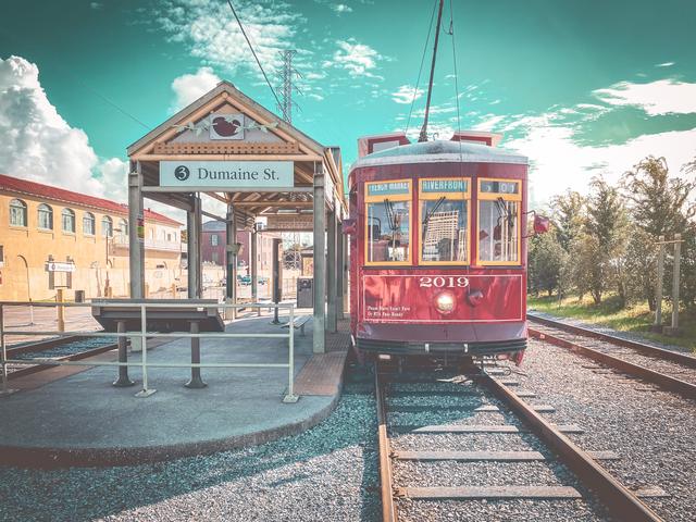 Red New Orleans streetcar at a stop under a bright sky