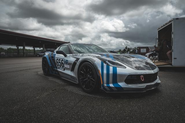 Wide-angle shot of a white and blue Corvette track car beneath brooding clouds